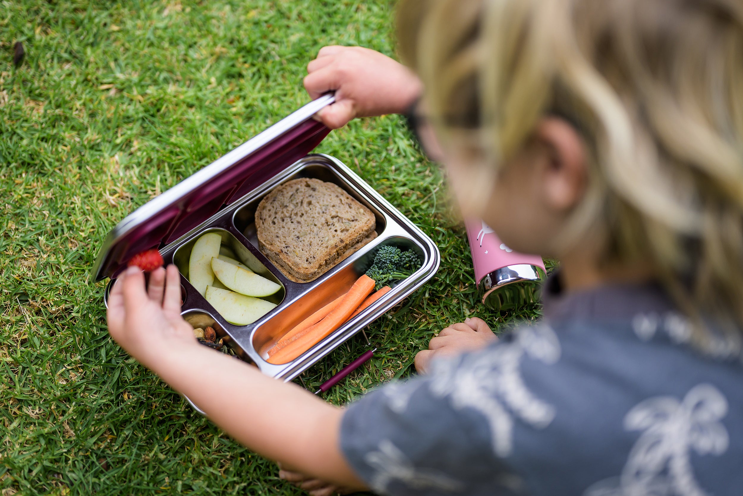 Child grabbing food from stainless leak proof lunchbox