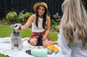 Two women having a picnic with a dog showing reusable water bottles from CaliWoods