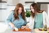 Two women smiling making granola on a reusable Baking Mat