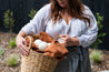 Woman outside holding a washing basket with a rust coloured towel and 3 wool Dryer Balls on top