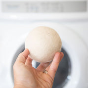 One Dryer Ball being held in a hand in front of a laundry