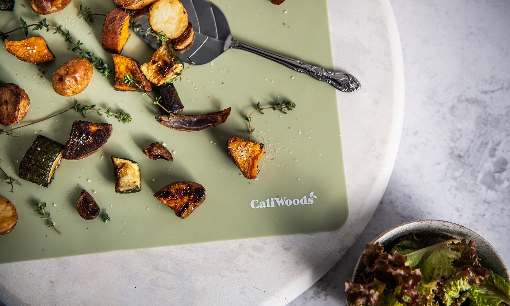 Roast vegetables with salt and thyme on a kitchen bench with a green Reusable Baking Mat