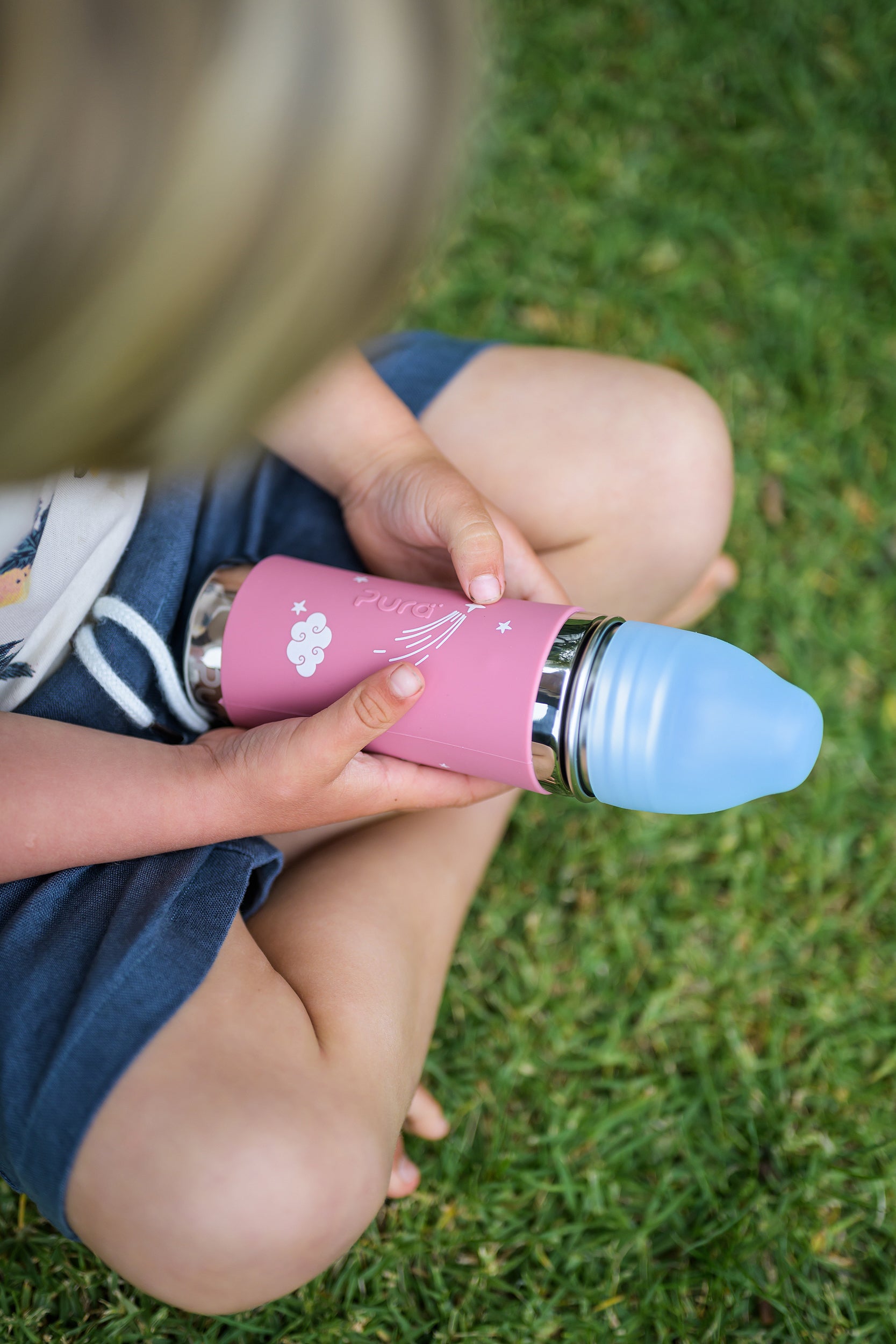 Pink pura water bottle held in the hands of a boy sitting cross legged 