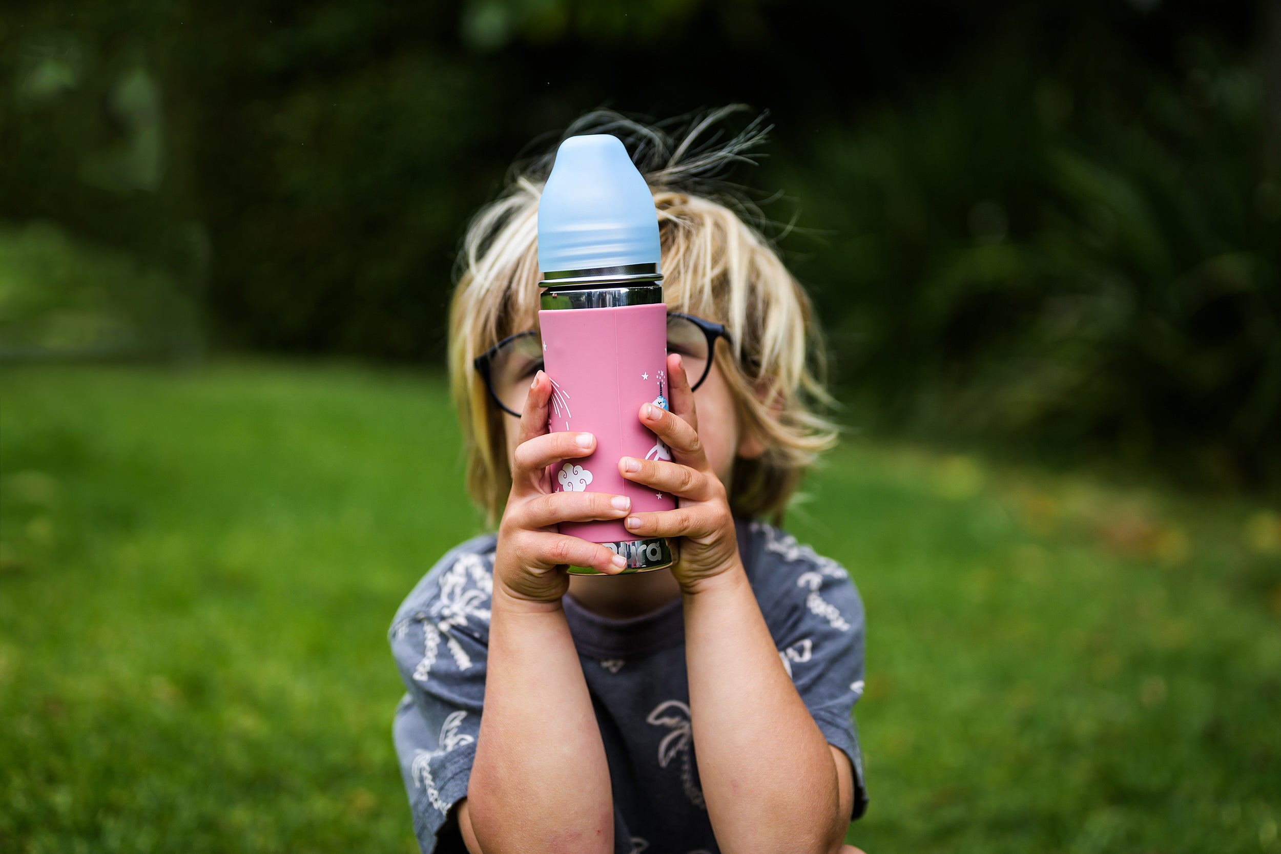 Boy holding pink unicorn CaliWoods stainless steel water bottle while sitting on the grass