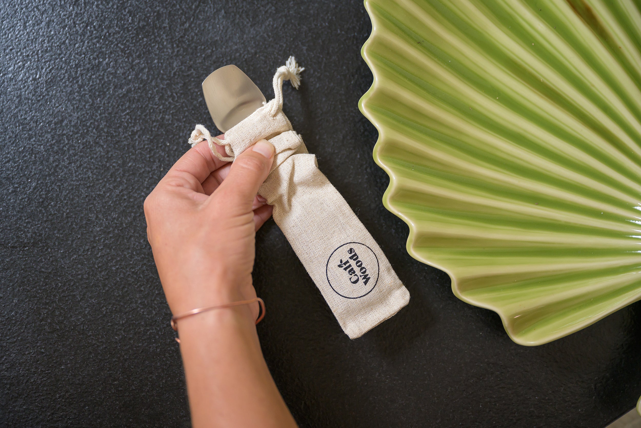 CaliWoods Stainless Steel Spork on a black bench with a green textured plate to the right