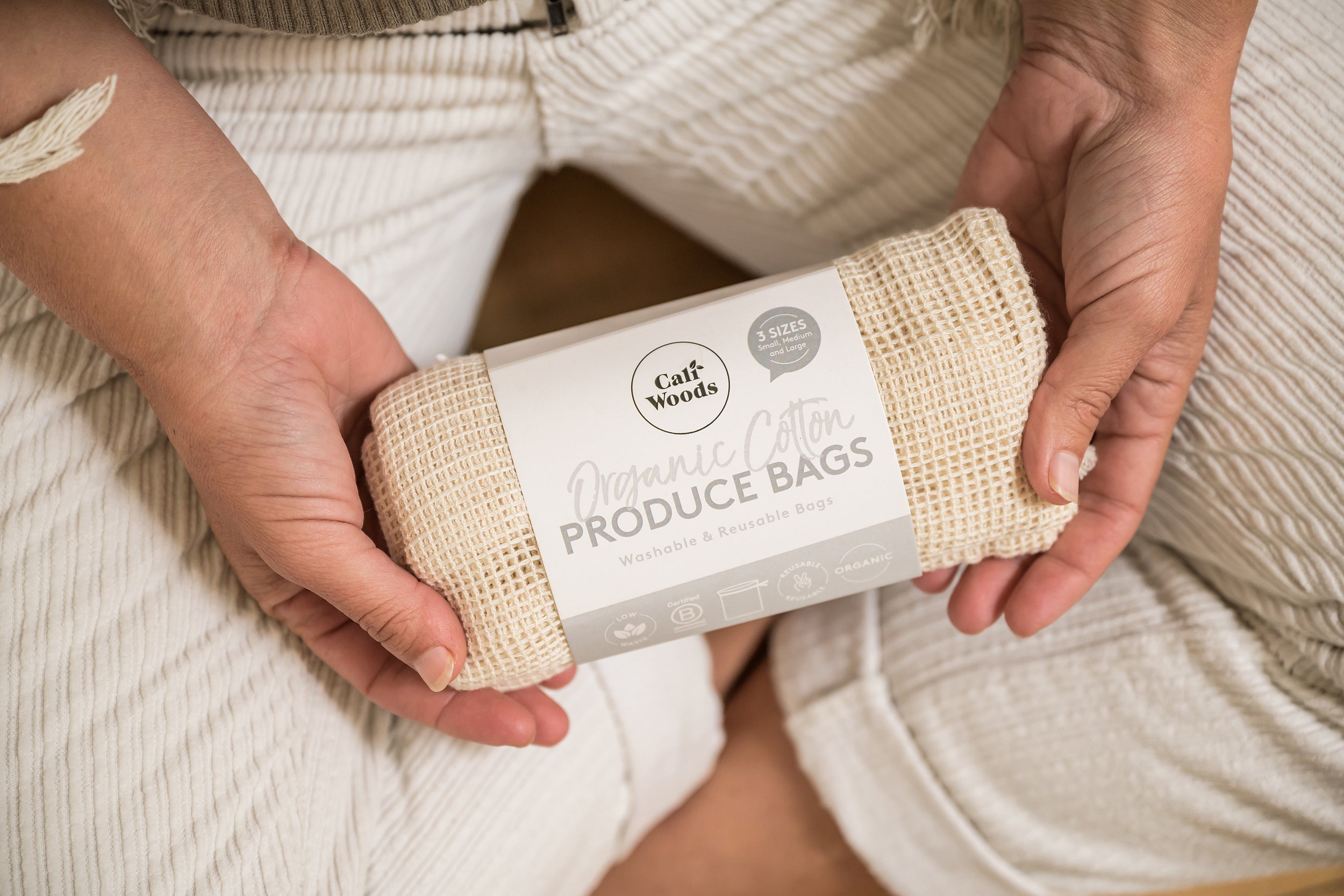 CaliWoods reusable produce eco bags held in hands with cross legs visible 