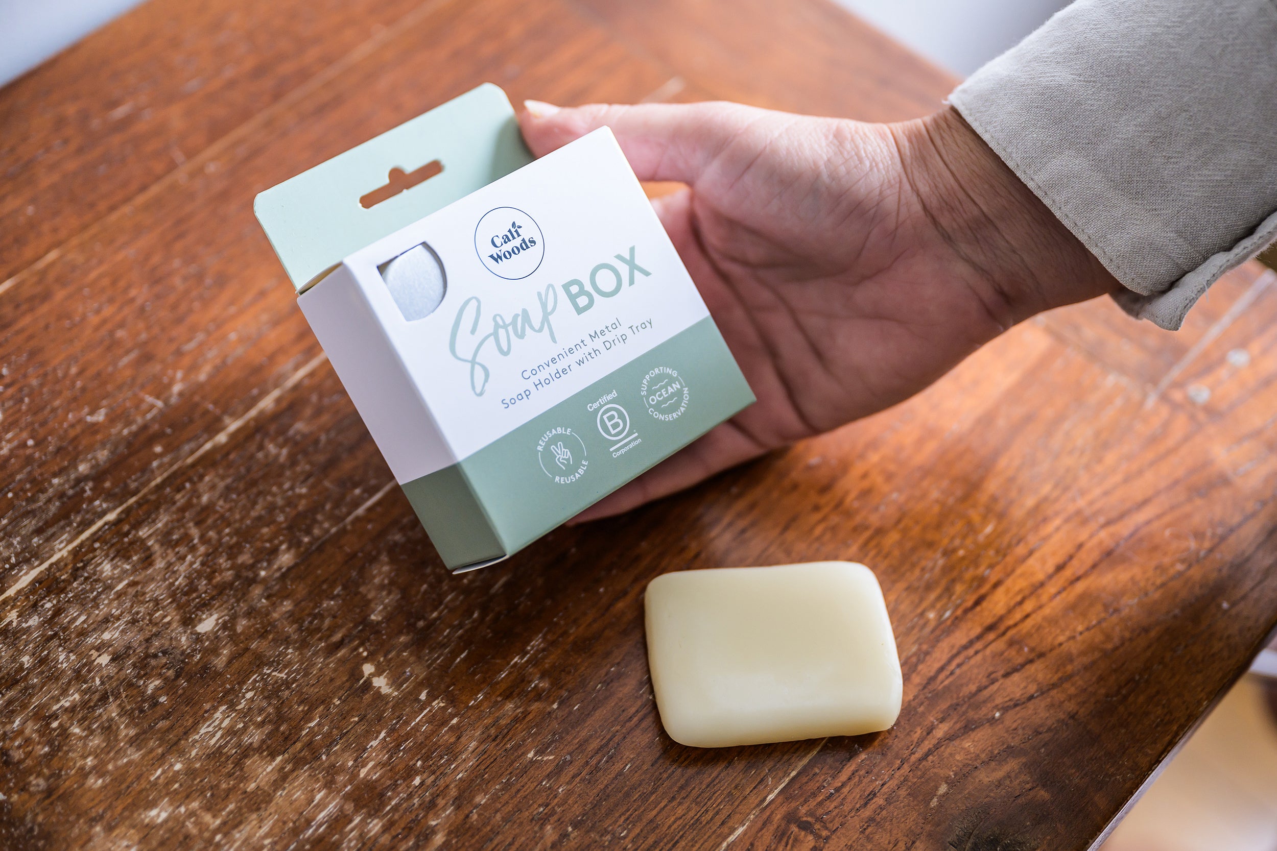 CaliWoods Soap Box in hand with a loose soap bar on a wooden bench