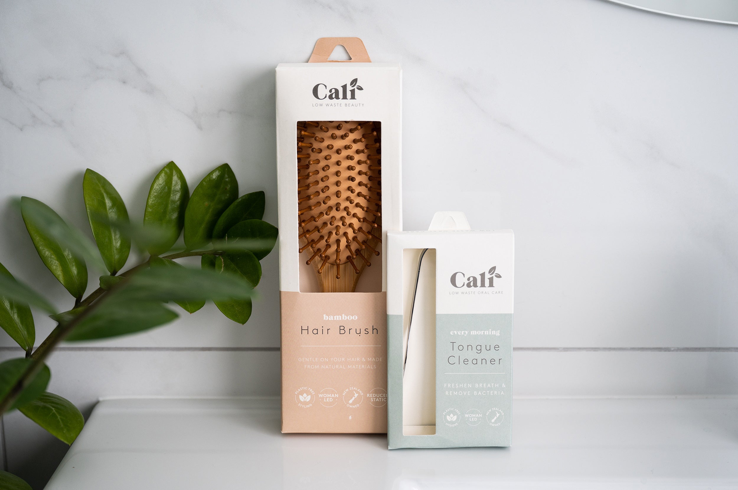 CaliWoods Tongue Cleaner with the CaliWoods Bamboo Hairbrush leaning against a wall