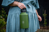 Woman in a blue dress holding a dark green Dawny Adventure Club CaliWoods reusable drink bottle