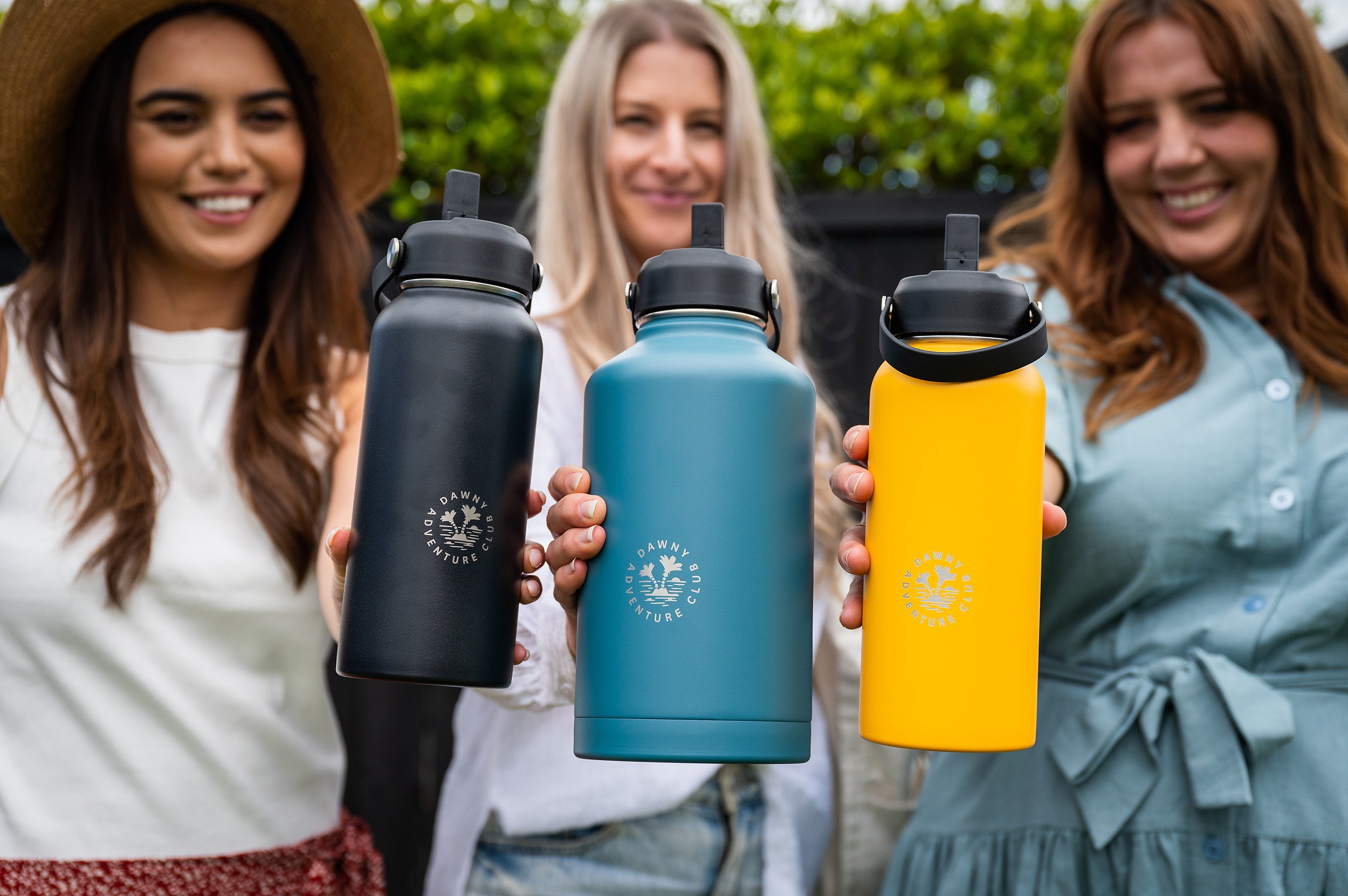 Three women holding out insulated water bottles in their hands