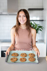 Smiling woman holding a baking tray with a Reusable Baking Mat with baked cookies on top 