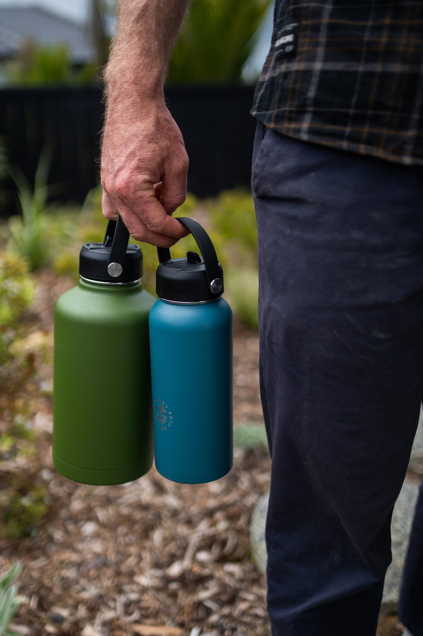 Man holding two Dawny reusable water bottles at his side with garden showing